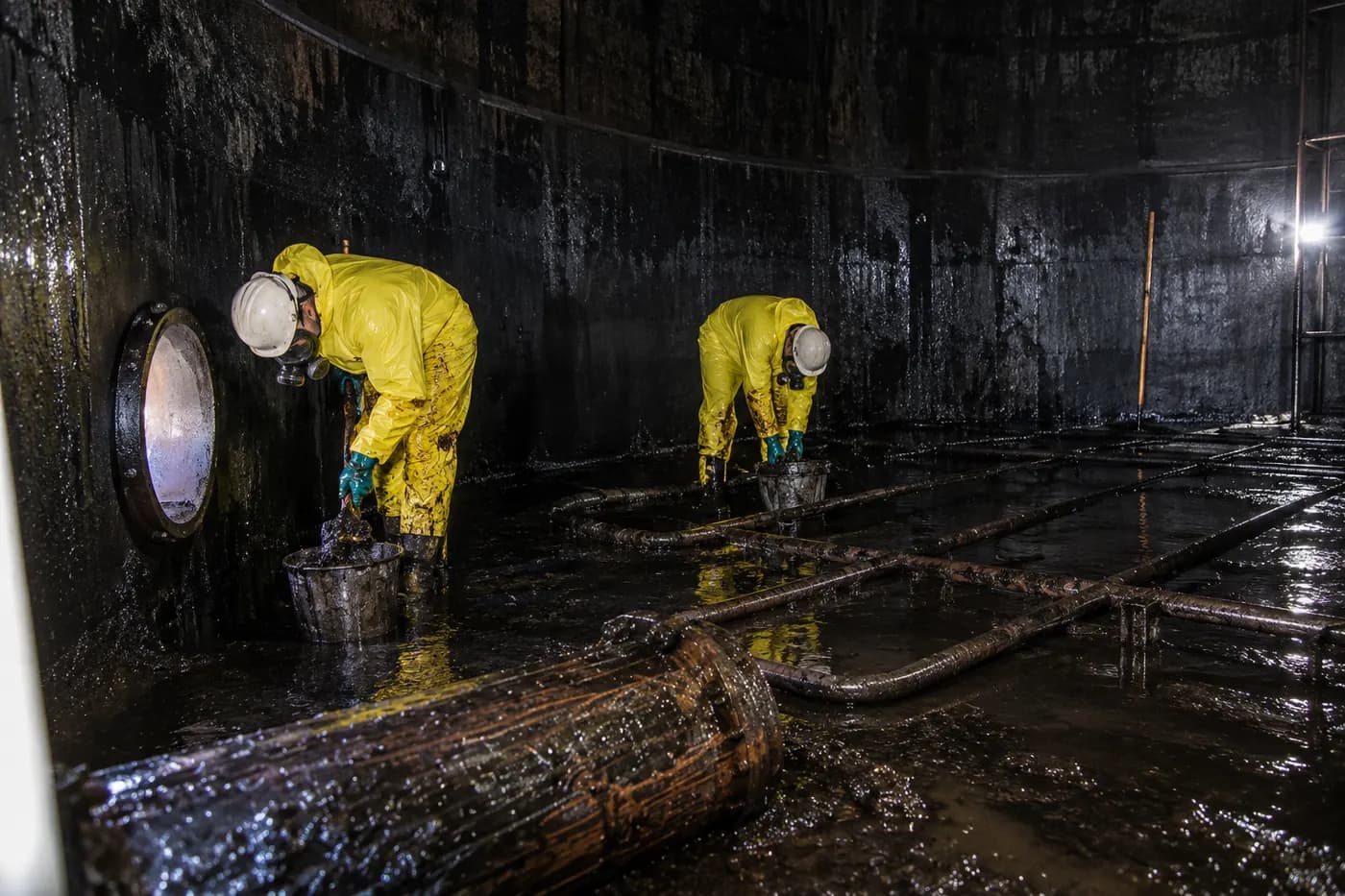 Clean Hub crew in protective suits and respirators removing sludge inside a large tank